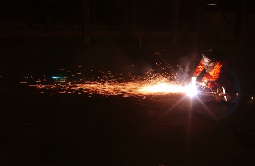 Welder working in the dark with a long trail of orange sparks
