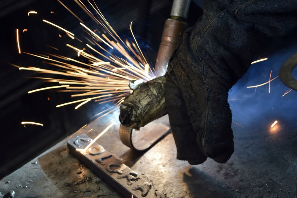 Gloved hand holding a welding torch with a burst of sparks