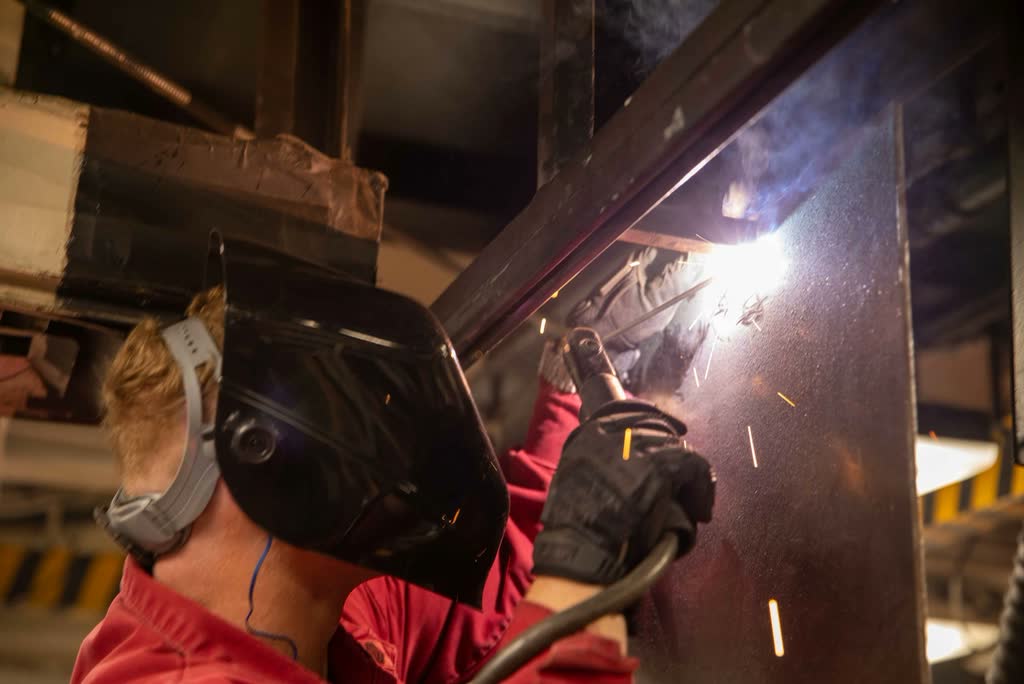 Welder in a protective mask working on a steel frame in a shower of sparks